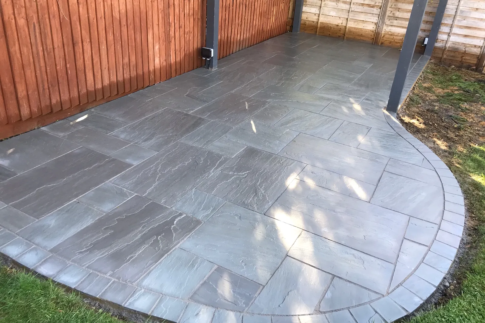 Sandstone patio with a curved setts edge beside a dark metal pergola frame, Marlow, 2020